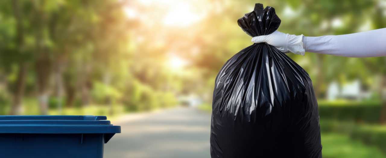 The garbage bag being held next to a recycling bin on a sunny street
