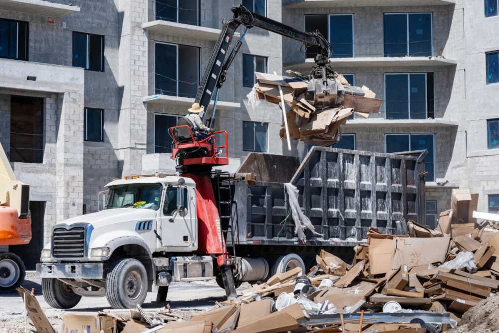 Cleanup and debris removal, heavy equipment with jawbone bucket used to pickup debris and deposit in commercial dump truck for hauling away, in residential building construction site