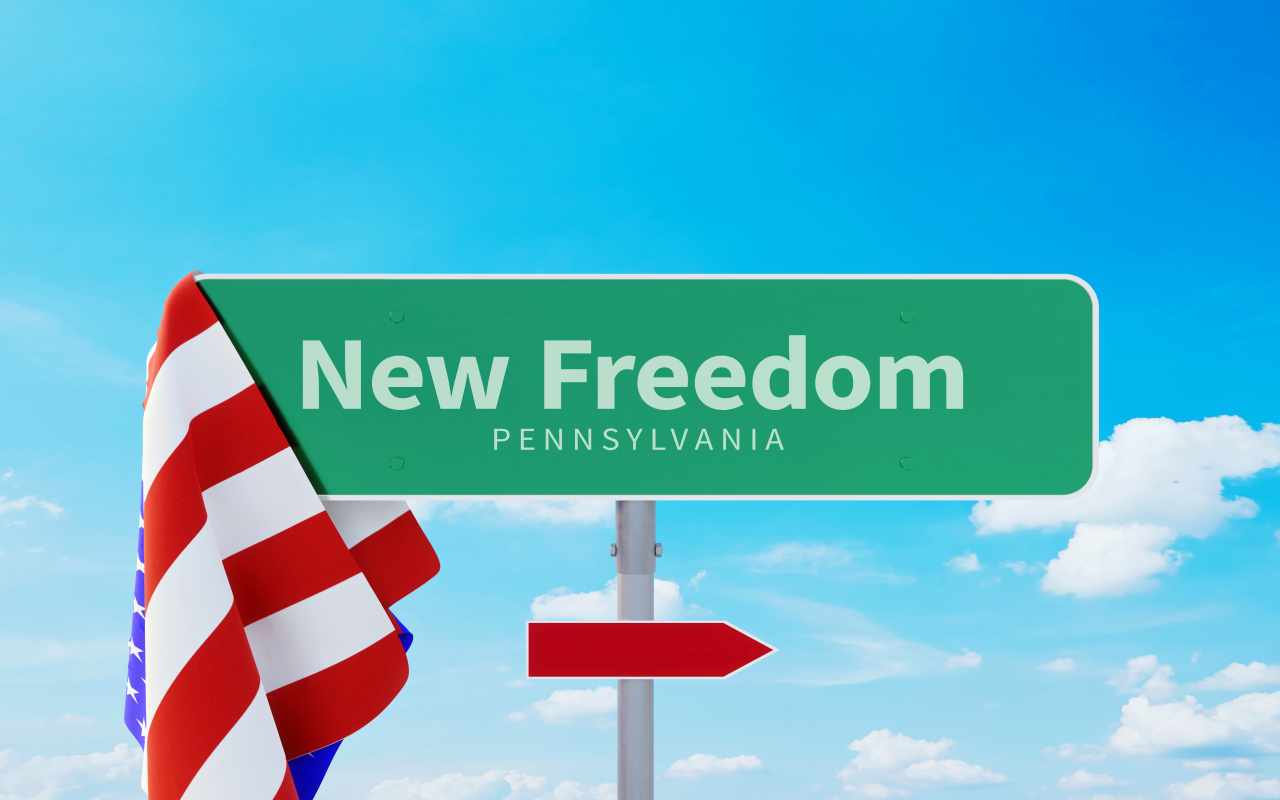 New Freedom &ndash; Pennsylvania. Road or Town Sign. Flag of the united states. Blue Sky. Red arrow shows the direction in the city. 
