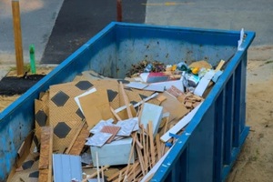 construction debris fills large blue waste dumpster near street