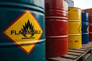 Hazardous Storage: Colorful barrels with flammable warning sign in industrial yard, chemical fuel drums, logistics and safety, toxic waste management concept