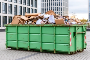 Green commercial roll-off dumpster overflowing with cardboard waste in a city business district