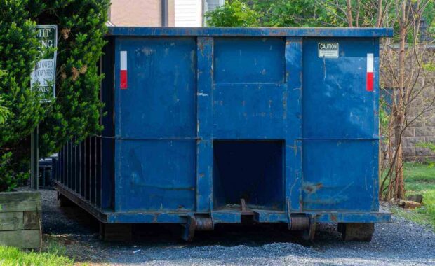 large weathered blue roll-off dumpster on a gravel driveway
