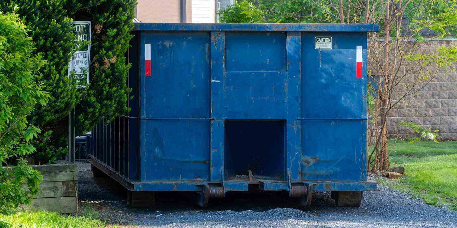 large weathered blue roll-off dumpster on a gravel driveway