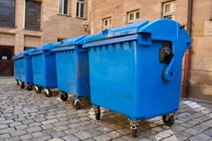 row of large blue plastic garbage bins on wheels standing on a cobblestone street