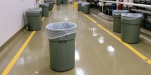 industrial hallway with multiple refuse bins lined along a clean, reflective floor