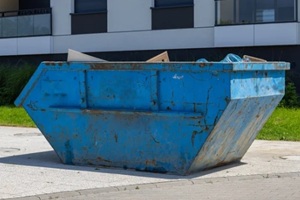 large blue metal construction dumpster placed near modern residential building on sunny day