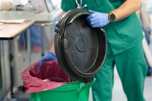 doctor wearing green scrubs opening biohazard medical waste container in hospital room