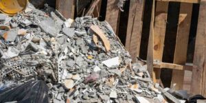 pile of broken concrete rubble and discarded building materials mixed with wooden planks and black trash bags inside the metal container