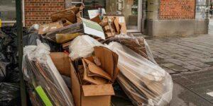stack of cardboard boxes and plastic trash bags placed on a New York City sidewalk near a brick building entrance