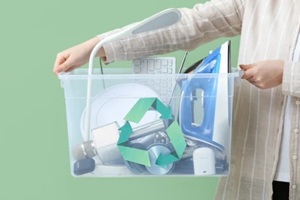 woman holding electronic waste for recycling in container on green background, closeup